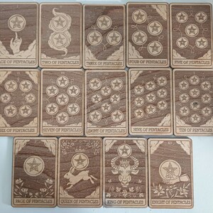 May include: A collection of wooden tarot cards featuring the suits of pentacles. Each card has a unique design with stars and symbols, and the card names are visible. The cards are arranged on a white surface.