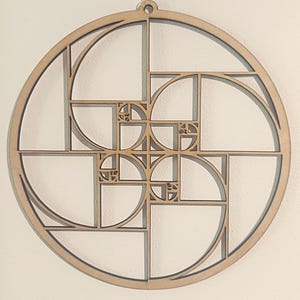 Könnte beinhalten: Eine Wanddekoration aus Holz mit der Fibonacci-Folge, einem mathematischen Muster aus Quadraten und Bögen, die in einer Spirale angeordnet sind. Die natürliche Holzfarbe bietet einen neutralen Ton, mit einem Loch zum Aufhängen.