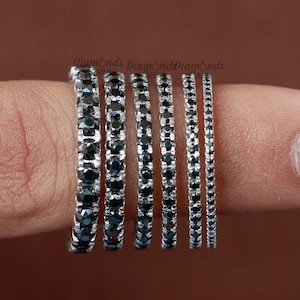 May include: A set of six silver eternity bands with black diamonds. The bands are stacked on a finger, with the largest band at the bottom and the smallest band at the top.