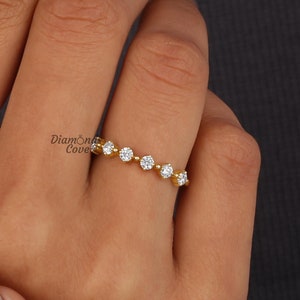 May include: A gold band ring with a row of small, round, clear gemstones. The ring is on a person's finger.