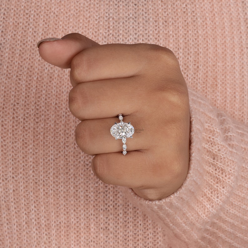 May include: A silver engagement ring with an oval-shaped center diamond and smaller diamonds set in a pave setting on the band.