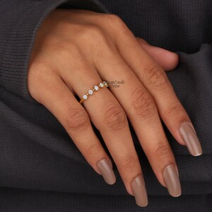 May include: A gold band ring with five small round diamonds set in a row. The ring is on a person's finger.