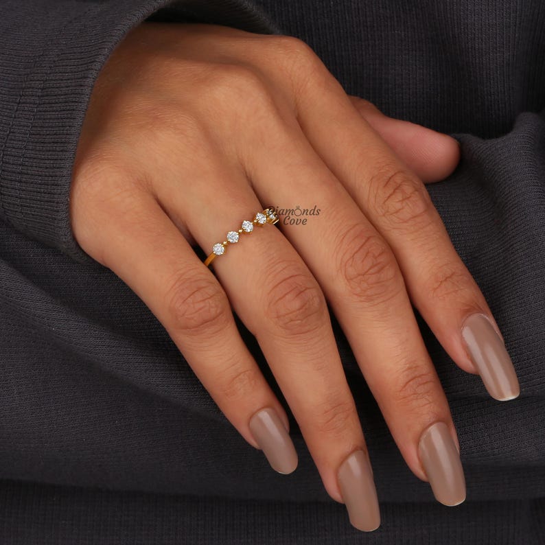 May include: A gold band ring with five small round diamonds set in a row. The ring is on a person's finger.
