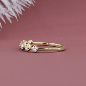 May include: A delicate gold band ring with five small round diamonds set in a row. The ring is on a pink background.
