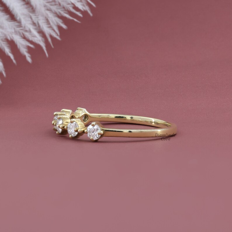 May include: A delicate gold band ring with five small round diamonds set in a row. The ring is on a pink background.