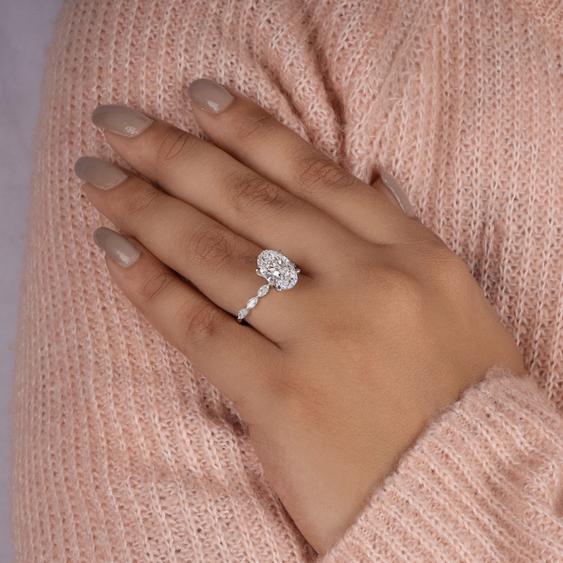 May include: A silver engagement ring with an oval-shaped center stone and a band adorned with smaller oval-shaped stones.