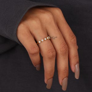 May include: A gold band ring with five small round diamonds set in a curved line. The ring is worn on the middle finger of a hand.