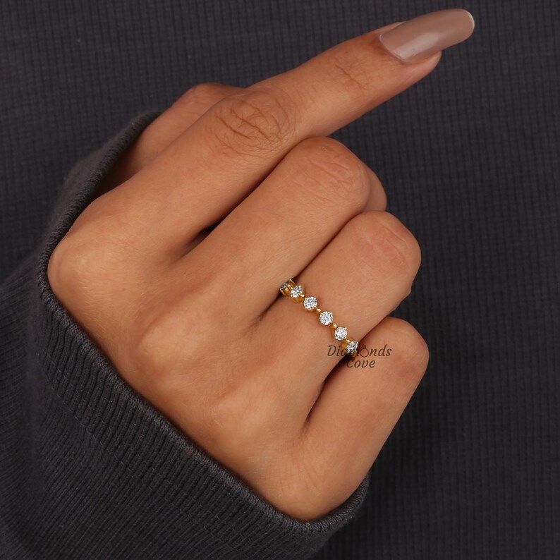 May include: A gold band ring with a row of small, round, clear stones. The ring is on a person's finger.