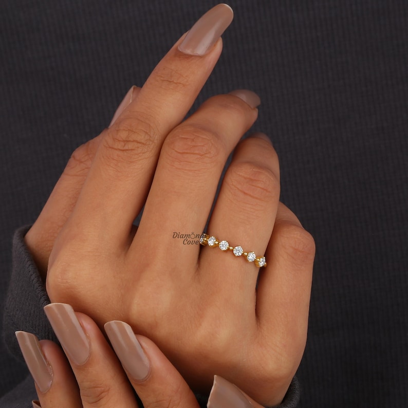 May include: A gold band ring with a row of small, round, clear gemstones. The ring is on a person's finger.