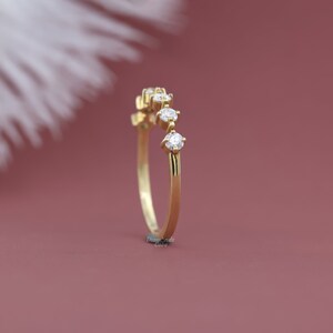 May include: A delicate gold band with five small round diamonds set in a curved line. The ring is on a pink background.