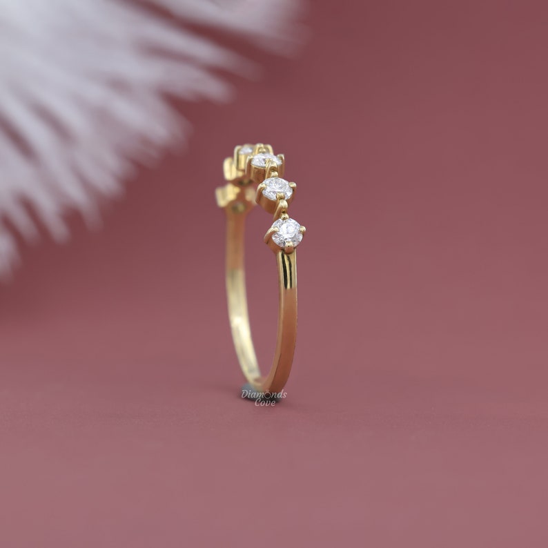 May include: A delicate gold band with five small round diamonds set in a curved line. The ring is on a pink background.
