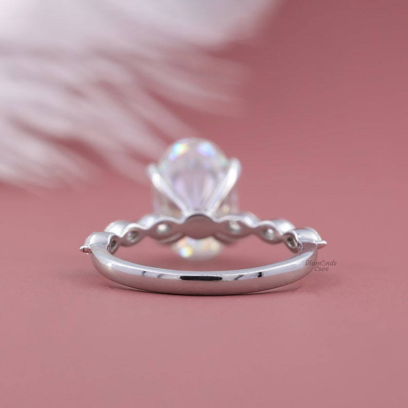 May include: A silver engagement ring with a large oval-shaped diamond. The ring has a delicate band with small diamonds on either side of the center stone.