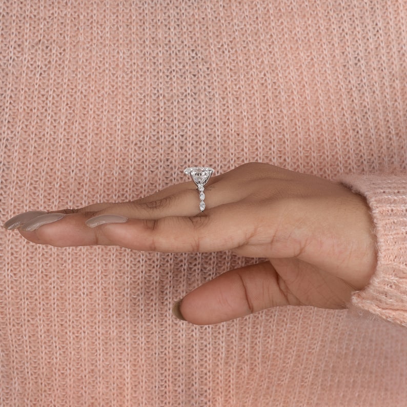 May include: A silver engagement ring with a large, oval-shaped center stone and smaller stones set in a halo around it. The band is also set with smaller stones.