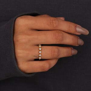 May include: A gold band ring with a row of small, clear round stones.