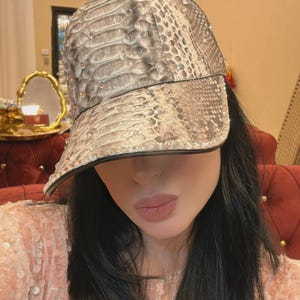 Può includere: Cappellino da baseball con motivo a pelle di serpente nei toni del grigio e del beige. Il cappellino ha una visiera nera ed è impreziosito da piccoli accenti scintillanti. Un accessorio di moda.