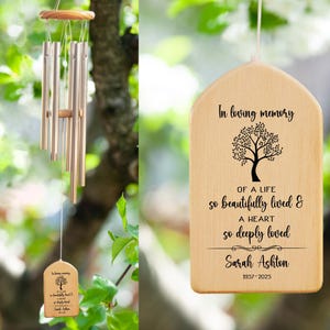 May include: A wooden wind chime with a personalized inscription that reads "In loving memory of a life so beautifully lived & a heart so deeply loved Sarah Ashton 1957-2025". The chime features a tree design and hangs from a string.