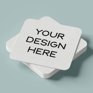 May include: A stack of white square coasters with rounded corners. The top coaster has the text "YOUR DESIGN HERE" printed in black.