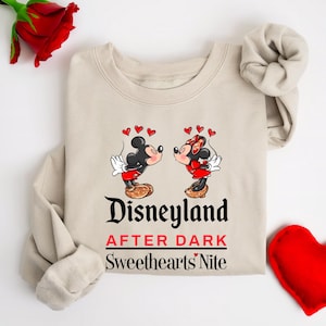 Puede incluir: Una sudadera beige con un gr&aacute;fico de Mickey Mouse y Minnie Mouse bes&aacute;ndose. El texto "Disneyland After Dark Sweethearts' Nite" est&aacute; impreso debajo del gr&aacute;fico.