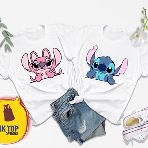 Op de afbeelding: Twee witte T-shirts met een cartoon afbeelding van Stitch en Angel uit de Disney-film Lilo & Stitch. De shirts liggen op een witte achtergrond met een blauwe jeans en witte sneakers.