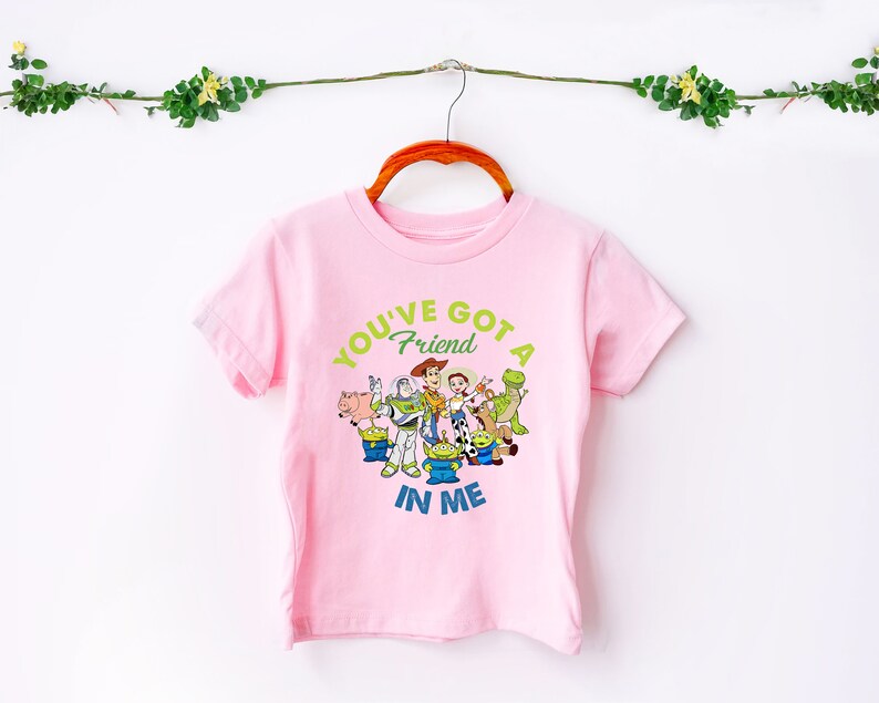 May include: Pink short-sleeved t-shirt featuring a graphic of the Toy Story characters. The text on the shirt reads "You've got a friend in me".