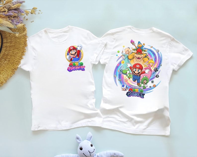 Peut inclure: Deux t-shirts blancs avec des graphiques du jeu vid&eacute;o "The Super Mario Galaxy". Un t-shirt a un petit graphisme de Mario sur le devant. L'autre t-shirt a un graphisme plus grand de Mario et d'autres personnages au dos.