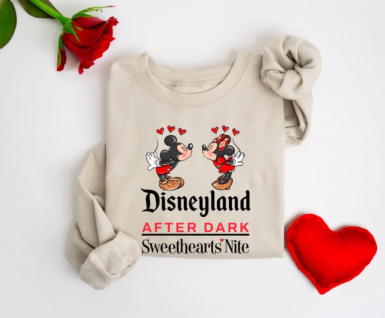 Puede incluir: Una sudadera beige con un gr&aacute;fico de Mickey Mouse y Minnie Mouse bes&aacute;ndose. El texto "Disneyland After Dark Sweethearts' Nite" est&aacute; impreso debajo del gr&aacute;fico.