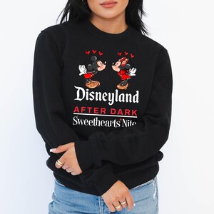 Puede incluir: Sudadera negra con un gr&aacute;fico de Mickey Mouse y Minnie Mouse bes&aacute;ndose. El texto "Disneyland After Dark Sweethearts Nite" est&aacute; impreso en la sudadera.
