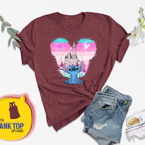 Op de afbeelding: Een maroon t-shirt met een blauw Stitch-personage uit Lilo & Stitch. Stitch staat voor een roze en blauw hartvormig ontwerp met een silhouet van Assepoester's kasteel. De tekst "WITH TANK TOP OPTIONS" staat in een gele spraakballon.
