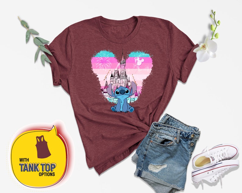 Op de afbeelding: Een maroon t-shirt met een blauw Stitch-personage uit Lilo & Stitch. Stitch staat voor een roze en blauw hartvormig ontwerp met een silhouet van Assepoester's kasteel. De tekst "WITH TANK TOP OPTIONS" staat in een gele spraakballon.