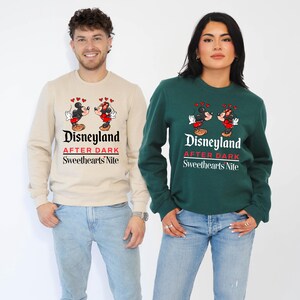 Puede incluir: Una pareja lleva sudaderas a juego con un gr&aacute;fico de Mickey Mouse y Minnie Mouse. Las sudaderas son beige y verde y dicen "Disneyland After Dark Sweethearts Nite".