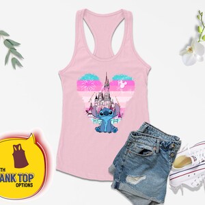Op de afbeelding: Een roze tanktop met een blauw Stitch-personage en een roze, blauw en wit hartvormig ontwerp met het kasteel van Assepoester. Het ontwerp bevat ook vuurwerk en een silhouet van Mickey Mouse.