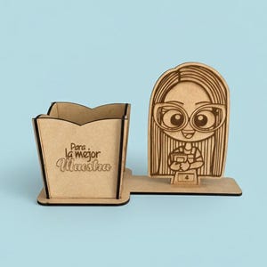 Puede incluir: Un organizador de escritorio de madera con un portalápices y un recorte decorativo de una maestra de dibujos animados con gafas. El portalápices tiene el texto "Para la mejor Maestra". El organizador es de madera marrón claro.