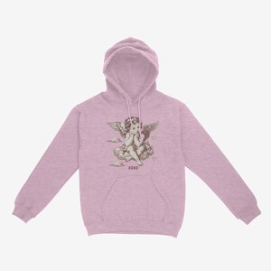 Pu&ograve; includere: Una felpa con cappuccio rosa chiaro con una grafica di un cherubino angelo con ali seduto su una nuvola. La grafica include il testo "XOXO".