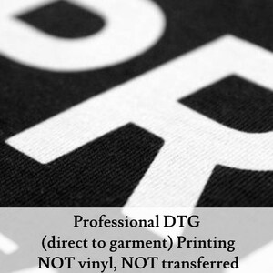 Pu&ograve; includere: Primo piano di testo bianco su tessuto nero che recita "Professional DTG (direct to garment) Printing NOT vinyl, NOT transferred".