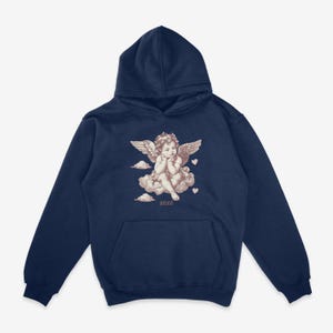 Pu&ograve; includere: Felpa con cappuccio blu navy con una grafica di un cherubino seduto su una nuvola con cuori e il testo "XOXO".