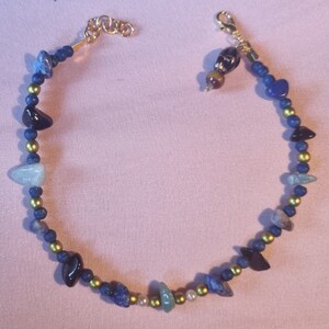 May include: A gold chain necklace with blue, green, black, and white stones. The necklace has a lobster clasp closure.