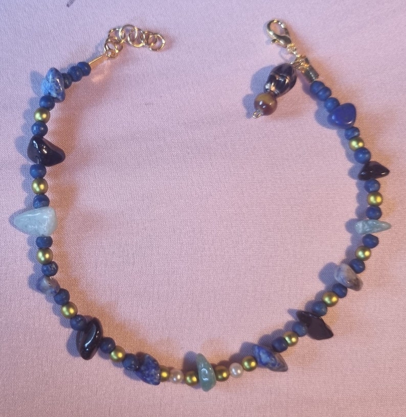 May include: A gold chain necklace with blue, green, black, and white stones. The necklace has a lobster clasp closure.