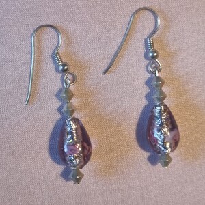 May include: A pair of silver dangle earrings with a teardrop-shaped purple glass bead accented with silver foil and pink flowers. The beads are strung on silver spacer beads.