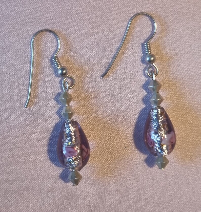 May include: A pair of silver dangle earrings with a teardrop-shaped purple glass bead accented with silver foil and pink flowers. The beads are strung on silver spacer beads.