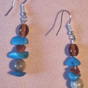 May include: A pair of silver dangle earrings with a layered design. The earrings feature brown, blue, and grey stones.