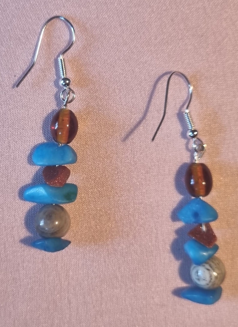 May include: A pair of silver dangle earrings with a layered design. The earrings feature brown, blue, and grey stones.