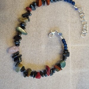 May include: A bracelet made with black, red, green, and pink stones, with a silver clasp and blue string.