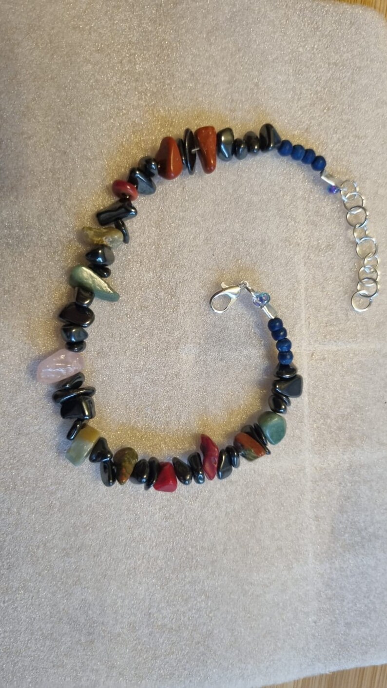May include: A bracelet made with black, red, green, and pink stones, with a silver clasp and blue string.