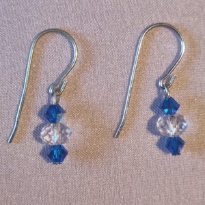 May include: A pair of silver dangle earrings with three crystal beads each. The top and bottom beads are dark blue, and the middle bead is clear.