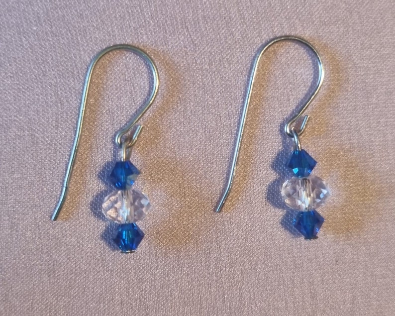 May include: A pair of silver dangle earrings with three crystal beads each. The top and bottom beads are dark blue, and the middle bead is clear.