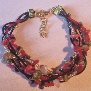 May include: Multi-strand bracelet with red, pink, green, and black beads and stones. The bracelet has a gold clasp and is made of black cord.