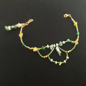 May include: A delicate gold chain anklet with green and white beads, featuring a butterfly-shaped design.