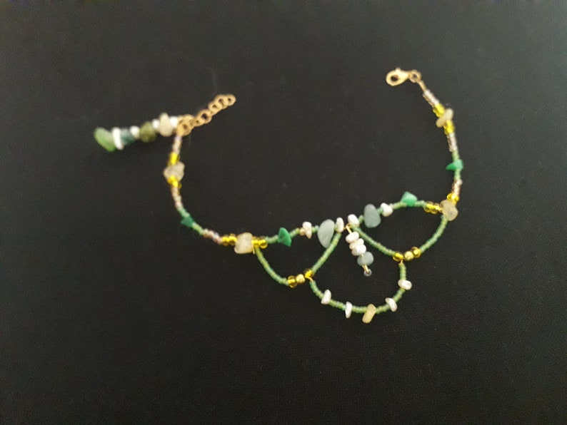May include: A delicate gold chain anklet with green and white beads, featuring a butterfly-shaped design.