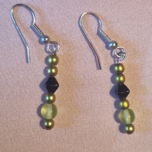 May include: A pair of dangle earrings with green and black beads. The earrings have silver hooks.