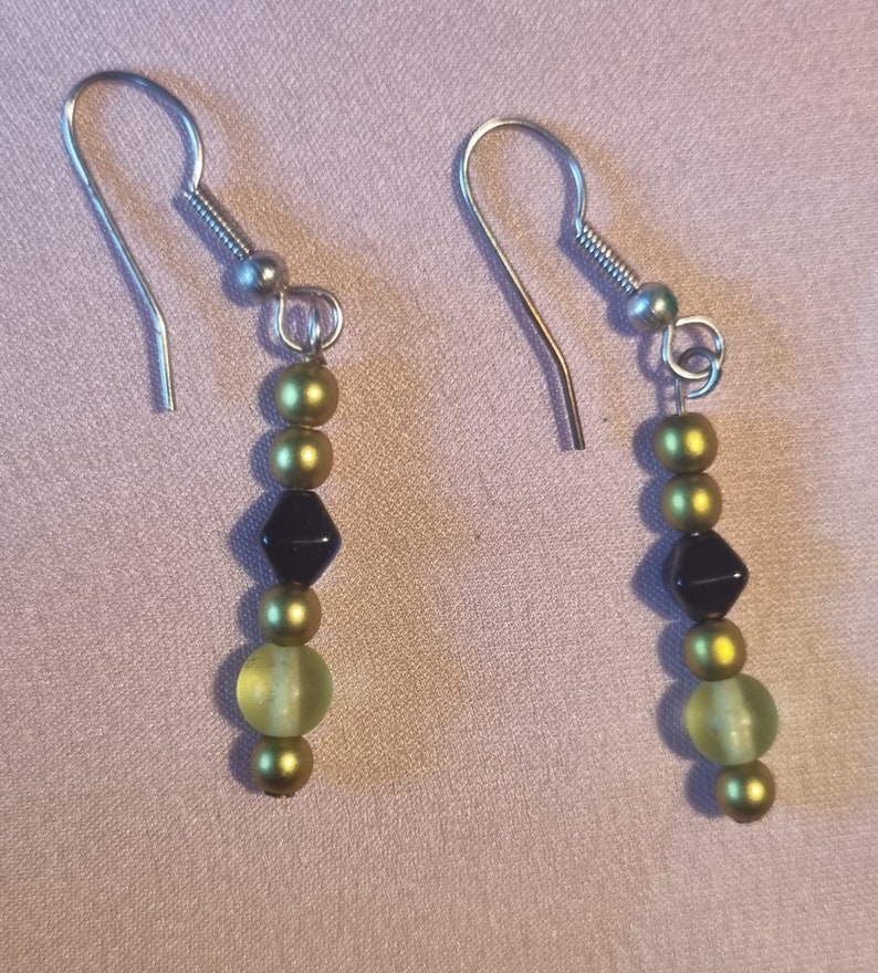 May include: A pair of dangle earrings with green and black beads. The earrings have silver hooks.